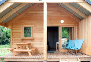 Houten chalet met terras, picknicktafel en twee blauwe stoelen bij Huttopia Divonne Les Bains in Frankrijk.