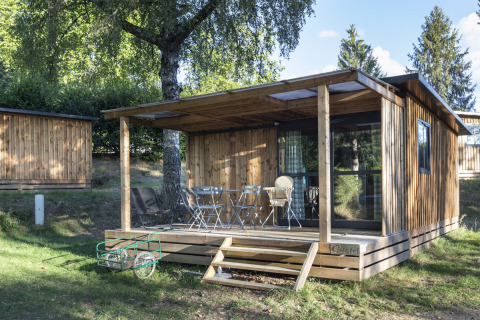 Træchalet med overdækket terrasse og havemøbler i det grønne landskab ved Huttopia Lac de la Siauve, Frankrig.