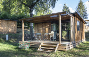 Holzchalet mit überdachter Terrasse und Gartenmöbeln in der Natur am Huttopia Lac de la Siauve, Frankreich.