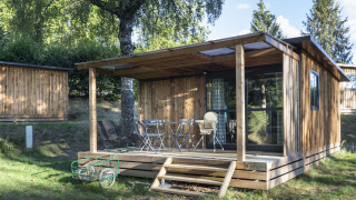 Houten chalet met overdekt terras en buitenmeubilair bij Huttopia Lac de la Siauve, Frankrijk, midden in de natuur.