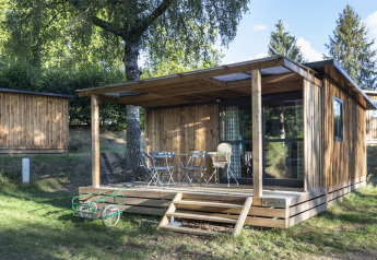 Houten chalet met overdekt terras en buitenmeubilair bij Huttopia Lac de la Siauve, Frankrijk, midden in de natuur.