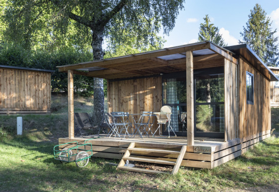 Houten chalet met overdekt terras en buitenmeubilair bij Huttopia Lac de la Siauve, Frankrijk, midden in de natuur.