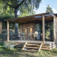Chalet in legno con terrazza coperta e arredo esterno a Huttopia Lac de la Siauve, Francia, immerso nella natura.