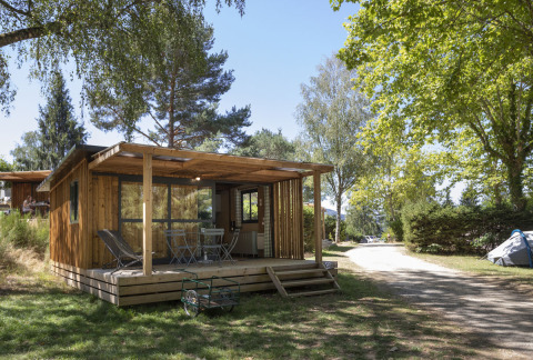 Chalet Evasion set fra forsiden med terrasse og havemøbler, omgivet af træer i et roligt naturområde.