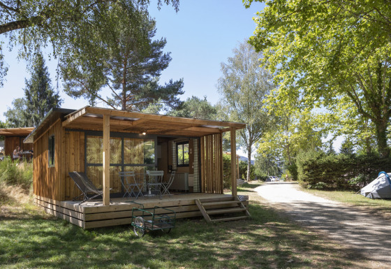 Vista frontal del Chalet Evasion con terraza de madera y muebles, rodeado de árboles en un entorno tranquilo.