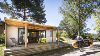 Una persona lleva una tabla de paddle frente a la cabaña Mobile home Vancouver con terraza y sillas.