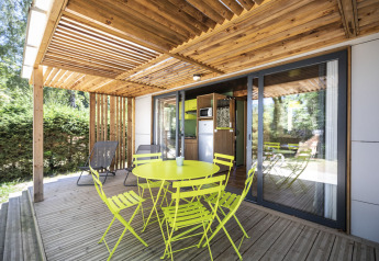 Overdekt houten terras met een felgele tafel en stoelen aan Mobile home Vancouver, Huttopia Lac de la Siauve, Frankrijk.