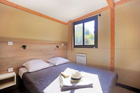 Innenaufnahme eines Schlafzimmers im Mobile Home Vancouver bei Huttopia Lac de la Siauve, Frankreich, mit Doppelbett.
