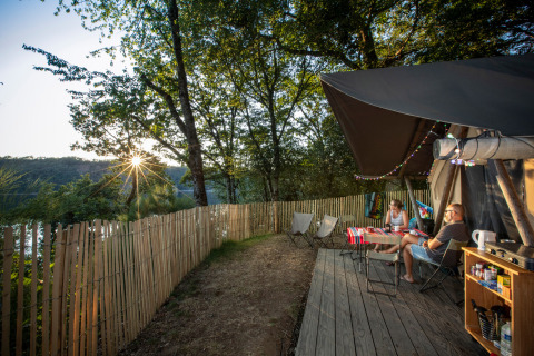 To personer sidder udenfor en Trapper Safari-telt ved Huttopia Lac de la Siauve, omgivet af natur og aftensol.