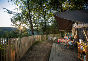 Zwei Personen entspannen an einem Trapper-Safarizelt im Huttopia Lac de la Siauve, umgeben von Bäumen und Abendsonne.