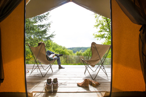 View from inside a safari tent onto a deck with chairs and shoes at Huttopia Lac de la Siauve, France.