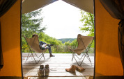 Vista dall’interno di una tenda safari su una terrazza con sedie e scarpe a Huttopia Lac de la Siauve, Francia.