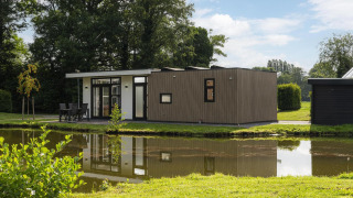 Moderna lodge The Water Lily vicino a uno stagno nel Holiday Park De Lochemse Berg, Paesi Bassi, immersa nel verde.
