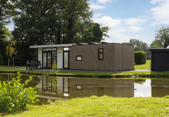 Moderna lodge The Water Lily vicino a uno stagno nel Holiday Park De Lochemse Berg, Paesi Bassi, immersa nel verde.