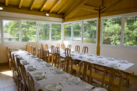 Sala da pranzo con tavoli lunghi apparecchiati al parco vacanze Camping Etxarri in Navarra, Spagna.