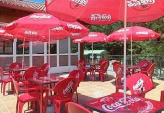Area esterna al Camping Etxarri in Navarra, Spagna, con sedie, tavoli e ombrelloni rossi Coca-Cola.