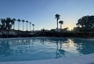 Sunset over the swimming pool at TAIGA Almeria Playa holiday park, with palm trees in Andalusia, Spain.