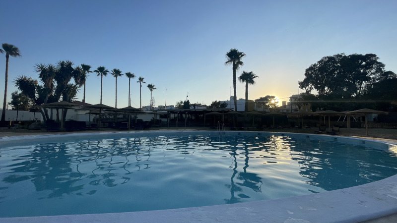 Sunset over the swimming pool at TAIGA Almeria Playa holiday park, with palm trees in Andalusia, Spain.