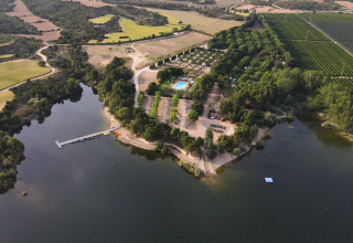 Vista aérea del parque vacacional TAIGA Lake Caspe en Aragón, España, con lago, bosque y piscina.