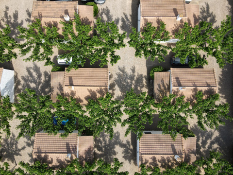Aerial view of cottages and leafy trees at TAIGA Lake Caspe holiday park in Aragón, Spain, casting shadows.