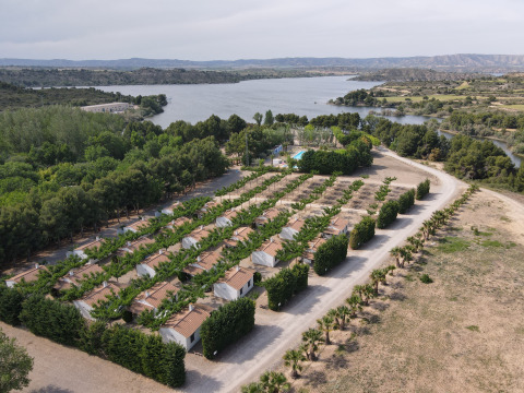 Vista aerea del villaggio TAIGA Lake Caspe in Aragona, Spagna, con bungalow immersi nel verde vicino al lago.