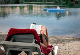 Person reading a book on a lounge chair by the shore at TAIGA Lake Caspe holiday park in Aragón, Spain.