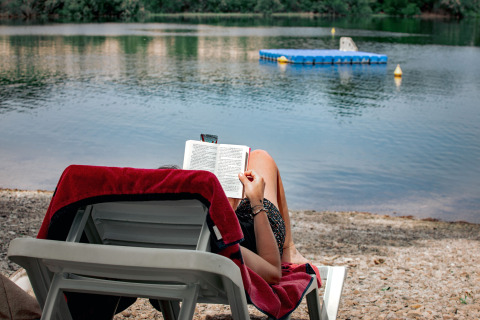 Person reading a book on a lounge chair by the shore at TAIGA Lake Caspe holiday park in Aragón, Spain.