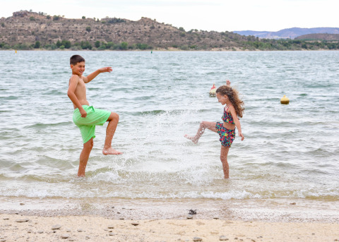 Dos niños juegan y salpican agua en el lago del parque vacacional TAIGA Lake Caspe en Aragón, España.