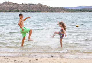 Dos niños juegan y salpican agua en el lago del parque vacacional TAIGA Lake Caspe en Aragón, España.