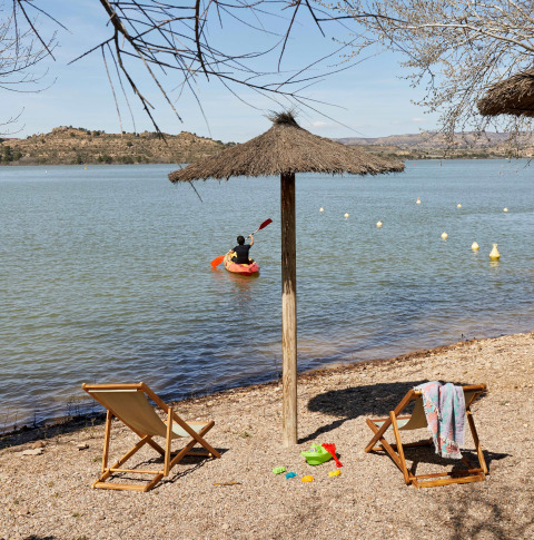 Playa en TAIGA Lake Caspe, parque vacacional en Aragón, España, con kayakista, tumbonas y sombrilla.