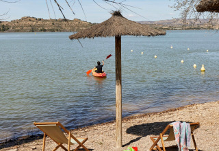 Plage du TAIGA Lake Caspe, parc de vacances en Aragón, Espagne, avec kayakiste, transats et parasol.
