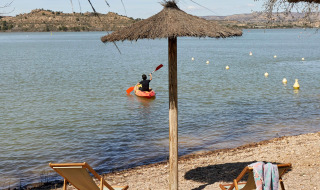Playa en TAIGA Lake Caspe, parque vacacional en Aragón, España, con kayakista, tumbonas y sombrilla.