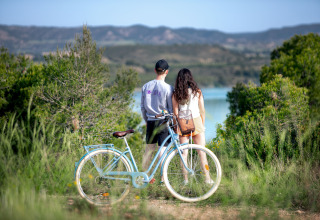 Twee personen staan naast een blauwe fiets en kijken uit over een meer in de natuur vlakbij Caspe, Aragón.