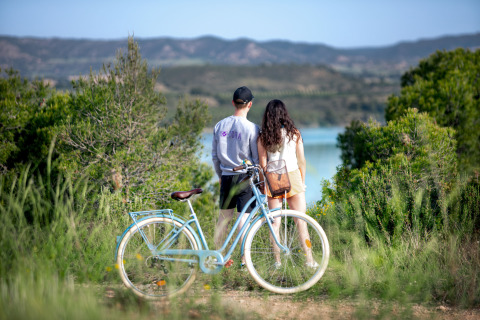 Zwei Personen stehen nebeneinander an einem blauen Fahrrad und blicken bei Caspe, Aragón, auf einen See.