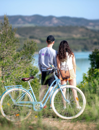 Dos personas junto a una bicicleta azul observan el paisaje natural cerca de Caspe, Aragón, España, junto al lago.