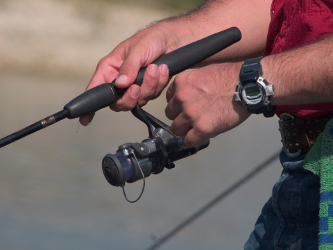 Persona che pesca vicino a Caspe, Aragón, Spagna, con una canna da pesca e un orologio sportivo digitale.