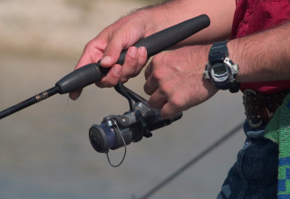 Persona pescando cerca de Caspe, Aragón, España, sujetando una caña de pescar y un reloj digital deportivo.