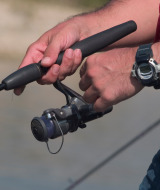 Persona pescando cerca de Caspe, Aragón, España, sujetando una caña de pescar y un reloj digital deportivo.