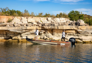 Two people fishing from a boat near the rocky shorelines of Caspe, Aragón, Spain on a sunny day.