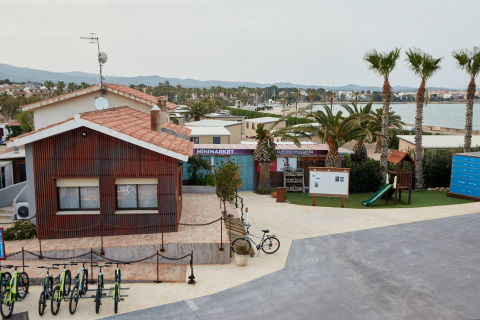 Vakantiepark met fietsen, minimarkt, speeltuin en palmbomen aan zee bij TAIGA Delta de l'Ebre, Catalonië.
