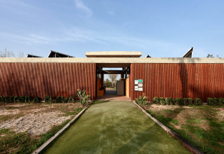 Eingang zum TAIGA Delta de l'Ebre Ferienpark in Katalonien, Spanien, mit Holzfassade und begrüntem Weg.