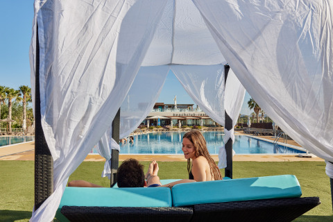 Zwei Personen entspannen unter einem Pavillon am Pool im TAIGA Delta de l'Ebre Ferienpark in Katalonien, Spanien.