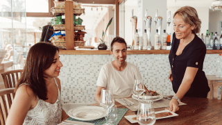 Dos personas disfrutan de una comida mientras una camarera sirve en el parque vacacional TAIGA Delta de l'Ebre.