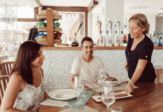 Zwei Gäste werden von einer freundlichen Kellnerin im Restaurant der TAIGA Delta de l'Ebre Ferienanlage bedient.