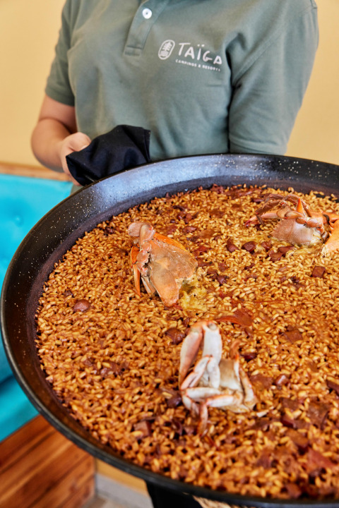 Un camarero sostiene una gran paellera con arroz y cangrejo, plato típico de L'Ampolla, Cataluña, España.