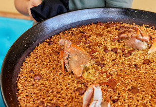 A server holds a large pan of rice and crab dish, typical of L'Ampolla in Catalonia, Spain, ready to serve.