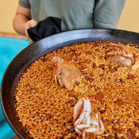Un camarero sostiene una gran paellera con arroz y cangrejo, plato típico de L'Ampolla, Cataluña, España.