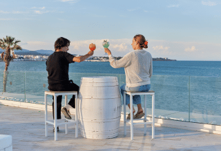 Dos personas brindan con bebidas junto al mar en el parque vacacional TAIGA Delta de l'Ebre, Cataluña.