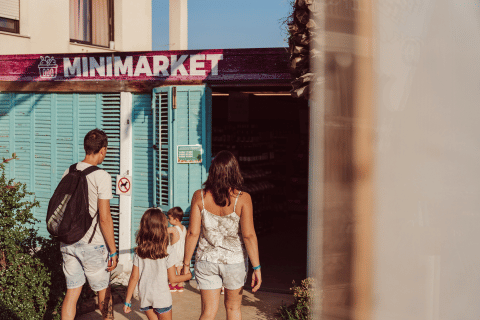 Een familie loopt een minimarkt binnen bij TAIGA Delta de l'Ebre vakantiepark in Catalonië, Spanje.