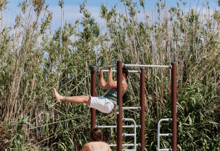 Dos personas hacen ejercicio en un gimnasio al aire libre sobre arena rodeados de cañas en Cataluña, España.